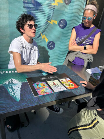 Marina Zurkow gestures, speaking, while an attendee looks on with folded arms