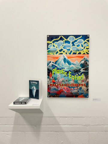 Enlarged "Plastic Eating Mushrooms" card and game play instruction booklet on display on gallery wall